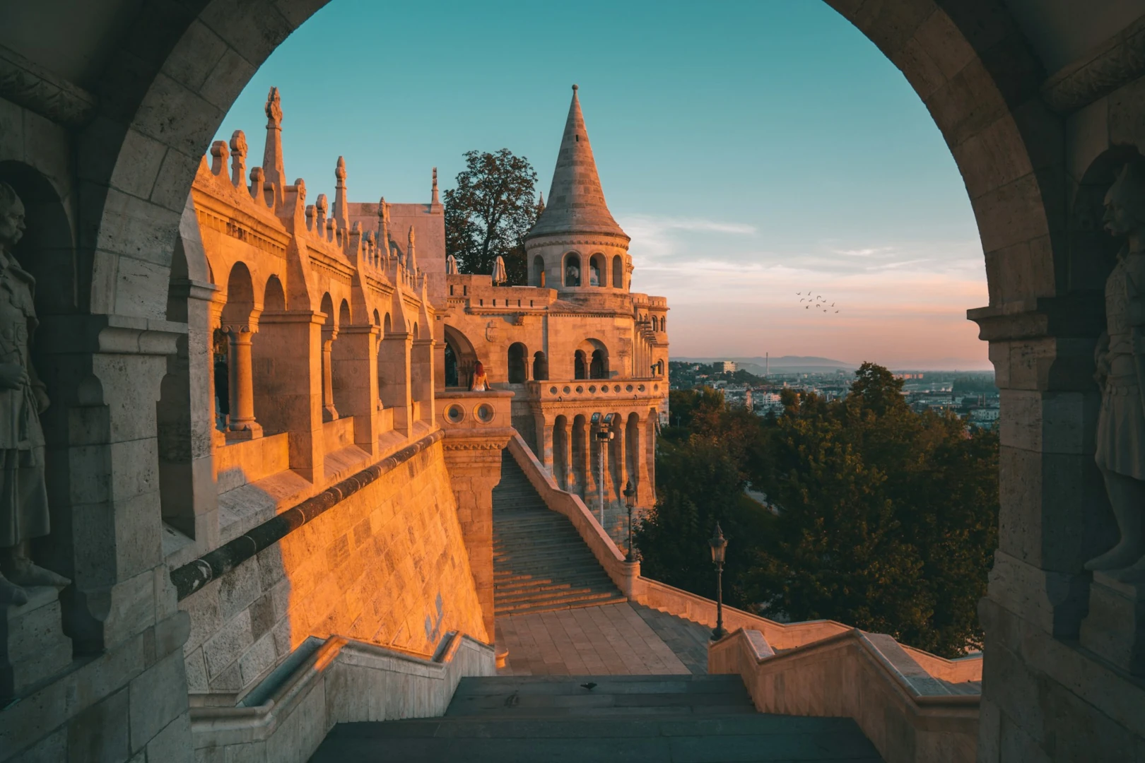 A medieval-style castle, with grand views over the Danube, glows orange in the light of the setting sun.