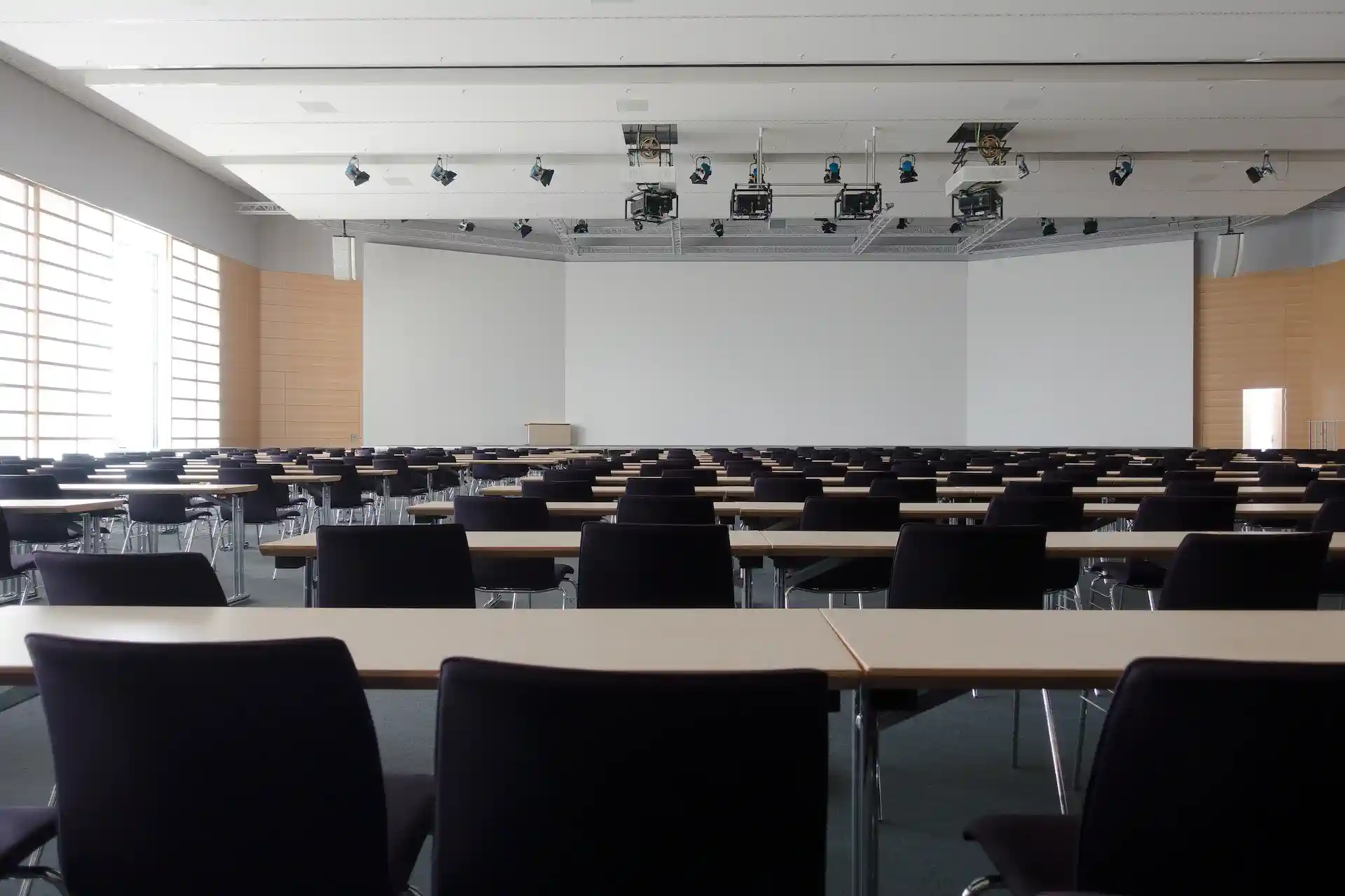 An image of an empty lecture theatre, taken from the back - whiteboards across the front wall, long wooden tables running in rows across the room, seats lined up ready to take students. 